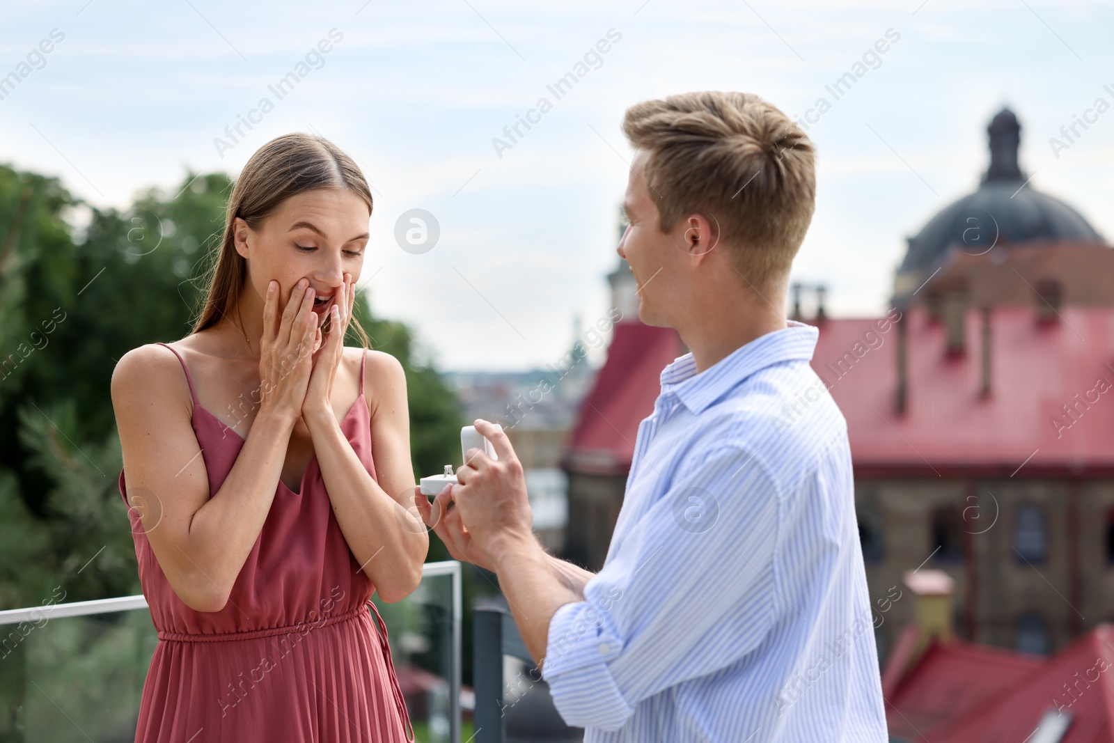 Man with engagement ring making marriage proposal to his surprised girlfriend on balcony outdoors Photo of Man with engagement ring making marriage proposal to his surprised girlfriend on balcony outdoors