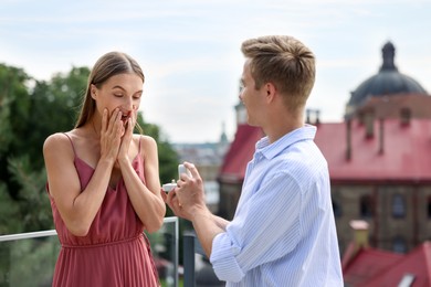 Photo of Man with engagement ring making marriage proposal to his surprised girlfriend on balcony outdoors