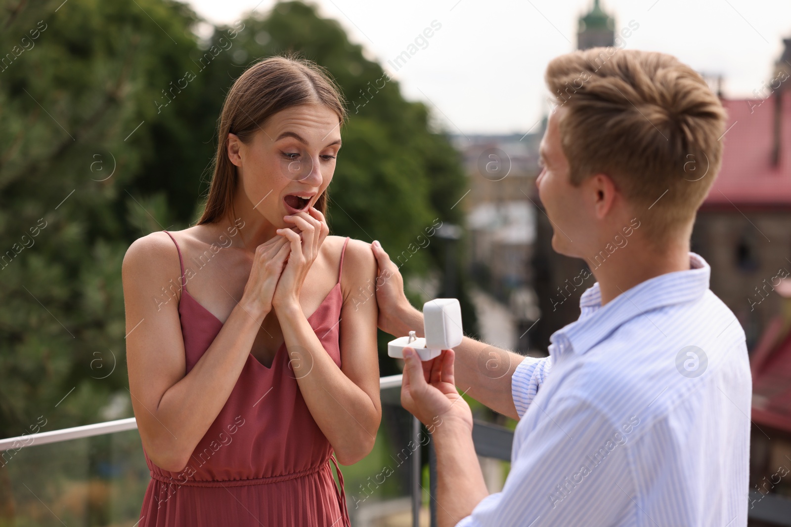 Man with engagement ring making marriage proposal to his surprised girlfriend on balcony outdoors Photo of Man with engagement ring making marriage proposal to his surprised girlfriend on balcony outdoors