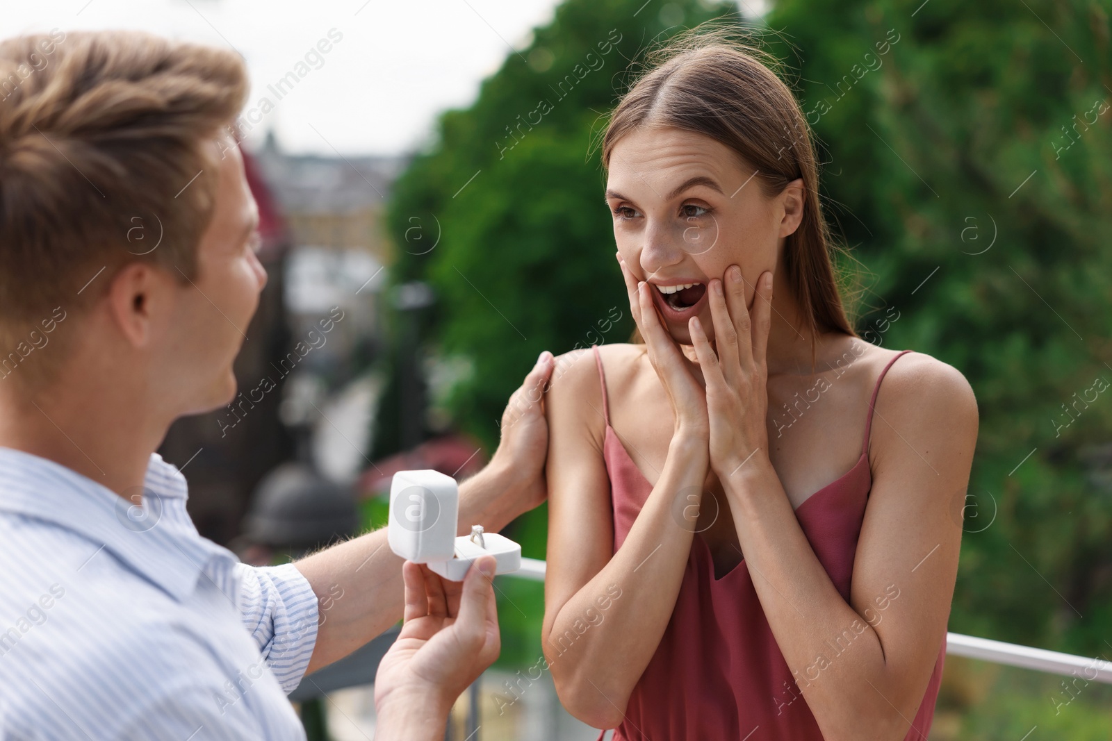 Man with engagement ring making marriage proposal to his surprised girlfriend on balcony outdoors Photo of Man with engagement ring making marriage proposal to his surprised girlfriend on balcony outdoors