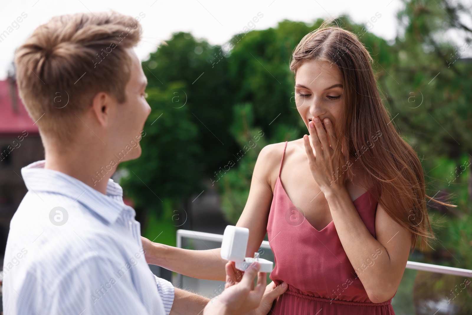 Man with engagement ring making marriage proposal to his surprised girlfriend on balcony outdoors Photo of Man with engagement ring making marriage proposal to his surprised girlfriend on balcony outdoors