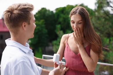 Photo of Man with engagement ring making marriage proposal to his surprised girlfriend on balcony outdoors
