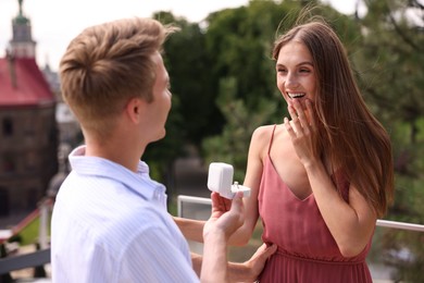 Photo of Man with engagement ring making marriage proposal to his happy girlfriend on balcony outdoors