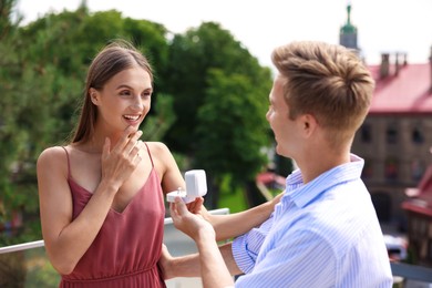 Photo of Man with engagement ring making marriage proposal to his happy girlfriend on balcony outdoors