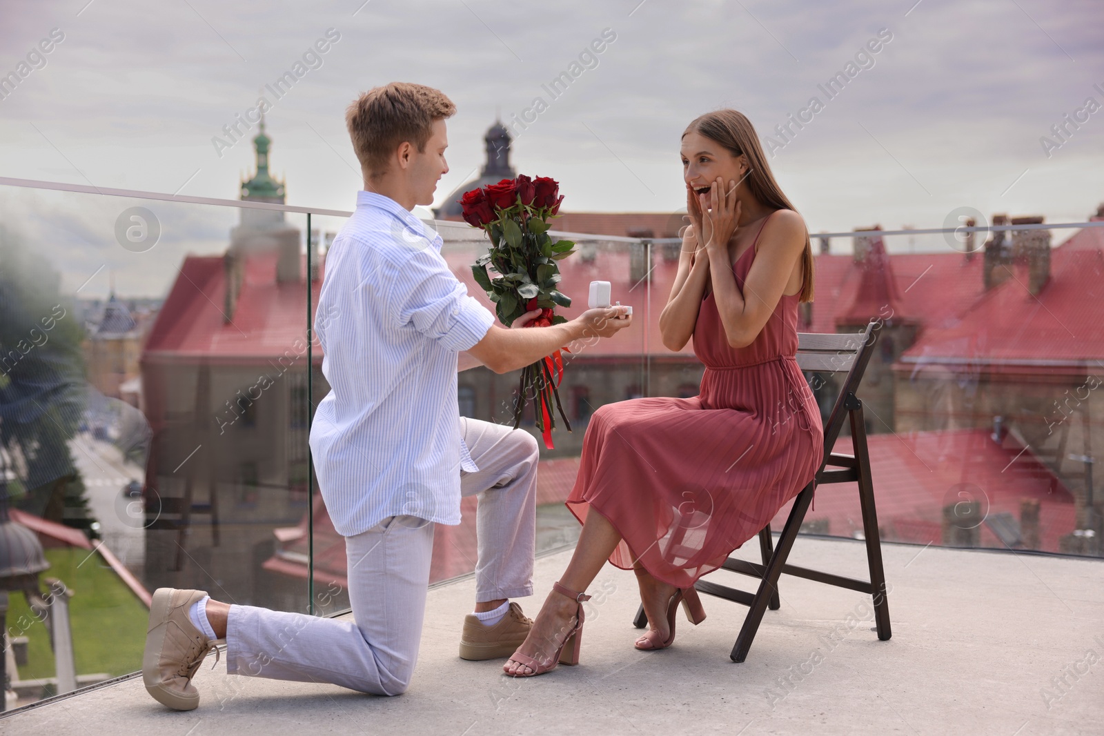 Man with engagement ring and bouquet of roses making marriage proposal to his happy girlfriend on balcony outdoors Photo of Man with engagement ring and bouquet of roses making marriage proposal to his happy girlfriend on balcony outdoors