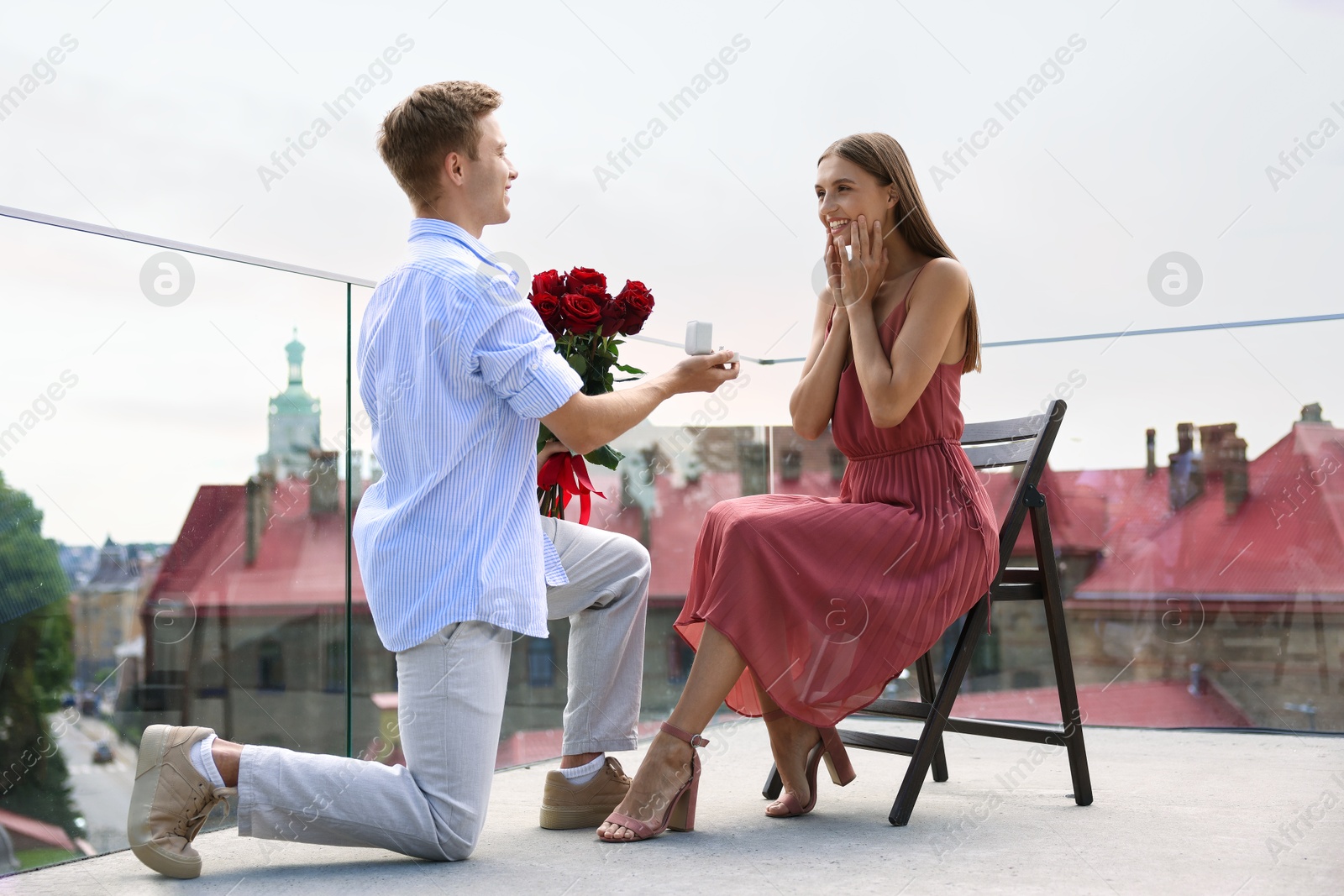 Man with engagement ring and bouquet of roses making marriage proposal to his happy girlfriend on balcony outdoors, low angle view Photo of Man with engagement ring and bouquet of roses making marriage proposal to his happy girlfriend on balcony outdoors, low angle view