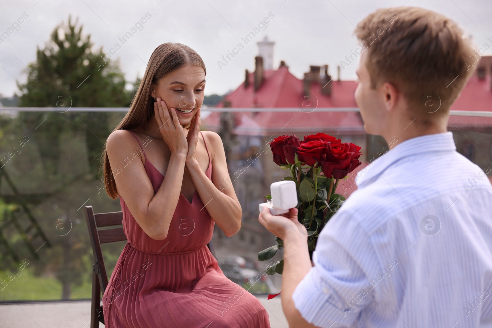 Man with engagement ring and bouquet of roses making marriage proposal to his happy girlfriend on balcony outdoors Photo of Man with engagement ring and bouquet of roses making marriage proposal to his happy girlfriend on balcony outdoors