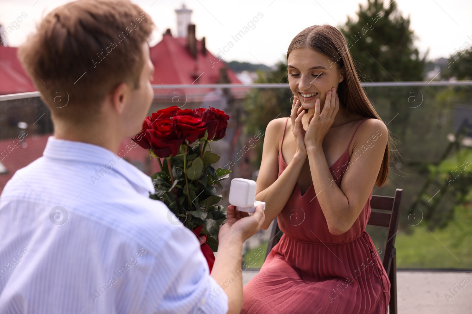 Man with engagement ring and bouquet of roses making marriage proposal to his happy girlfriend on balcony outdoors Photo of Man with engagement ring and bouquet of roses making marriage proposal to his happy girlfriend on balcony outdoors