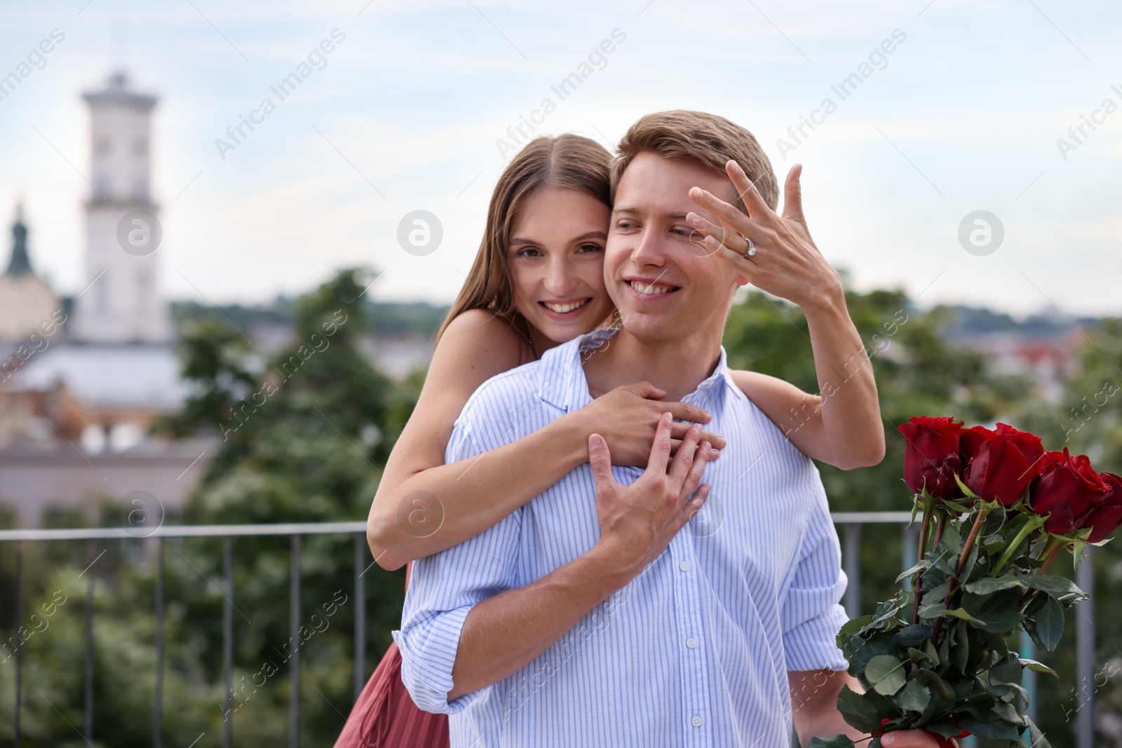 Marriage proposal. Smiling woman with engagement ring and her fiance holding bouquet of roses on balcony outdoors Photo of Marriage proposal. Smiling woman with engagement ring and her fiance holding bouquet of roses on balcony outdoors