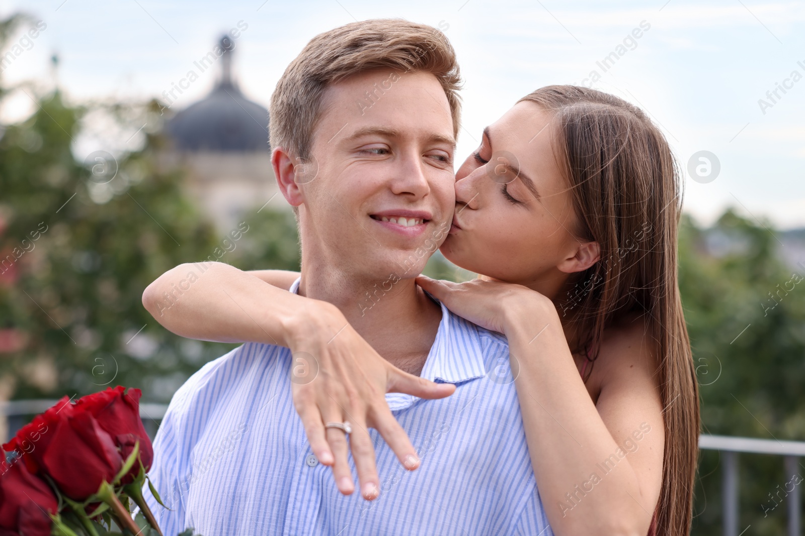 Marriage proposal. Woman with engagement ring kissing her fiance with bouquet of roses on balcony outdoors Photo of Marriage proposal. Woman with engagement ring kissing her fiance with bouquet of roses on balcony outdoors