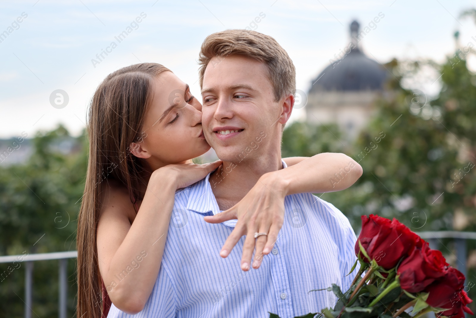 Marriage proposal. Woman with engagement ring kissing her fiance with bouquet of roses on balcony outdoors Photo of Marriage proposal. Woman with engagement ring kissing her fiance with bouquet of roses on balcony outdoors