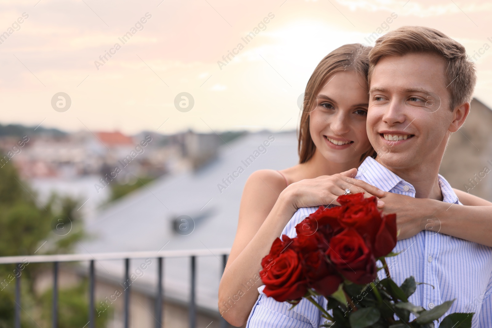 Marriage proposal. Smiling woman with engagement ring and her fiance holding bouquet of roses on balcony outdoors. Space for text Photo of Marriage proposal. Smiling woman with engagement ring and her fiance holding bouquet of roses on balcony outdoors. Space for text