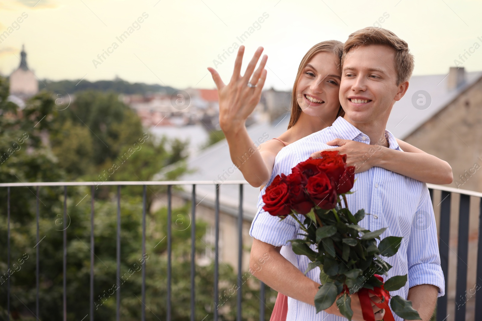Marriage proposal. Smiling woman showing engagement ring and her fiance holding bouquet of roses on balcony outdoors. Space for text Photo of Marriage proposal. Smiling woman showing engagement ring and her fiance holding bouquet of roses on balcony outdoors. Space for text