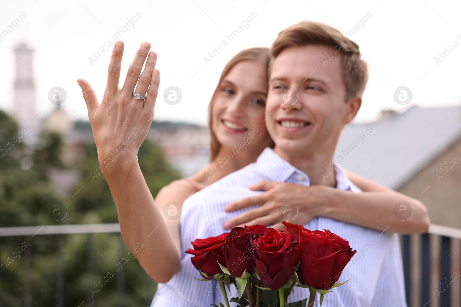 Marriage proposal. Smiling woman showing engagement ring and her fiance holding bouquet of roses on balcony outdoors, selective focus Photo of Marriage proposal. Smiling woman showing engagement ring and her fiance holding bouquet of roses on balcony outdoors, selective focus