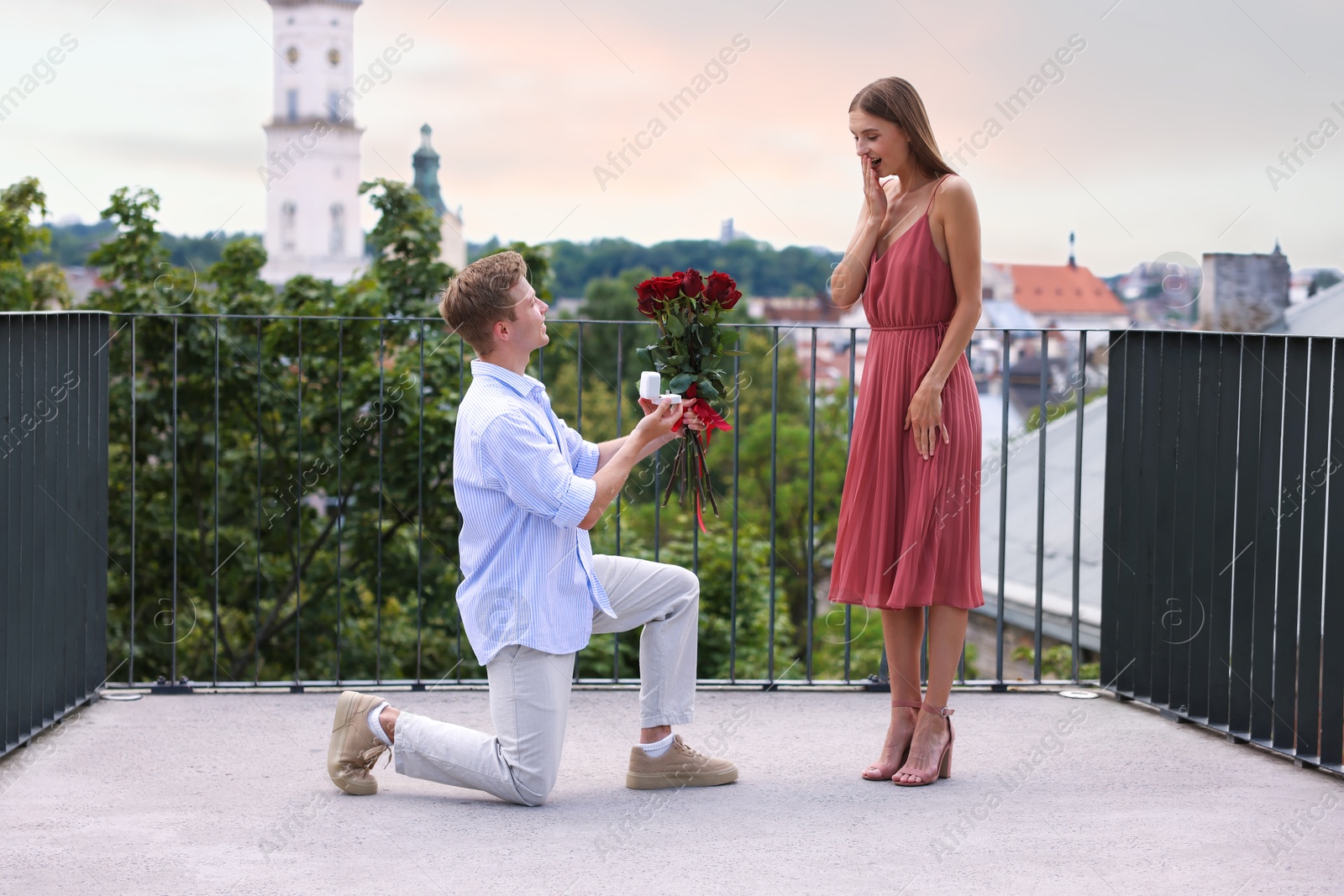 Man with engagement ring and bouquet of roses making marriage proposal to his happy girlfriend on balcony outdoors Photo of Man with engagement ring and bouquet of roses making marriage proposal to his happy girlfriend on balcony outdoors