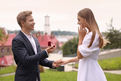 Photo of Smiling man with engagement ring making marriage proposal to his surprised girlfriend outdoors