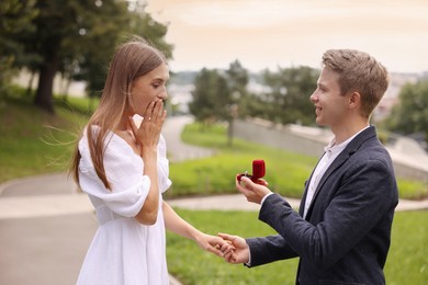 Photo of Smiling man with engagement ring making marriage proposal to his surprised girlfriend outdoors