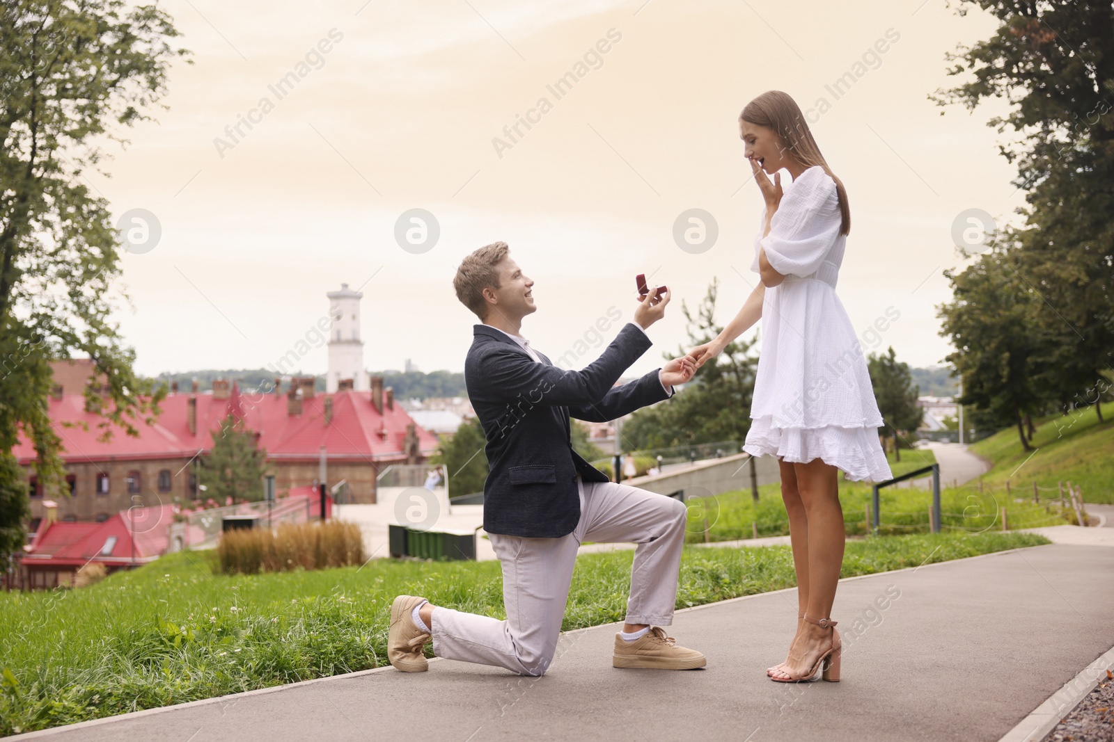 Smiling man with engagement ring making marriage proposal to his surprised girlfriend outdoors. Space for text Photo of Smiling man with engagement ring making marriage proposal to his surprised girlfriend outdoors. Space for text