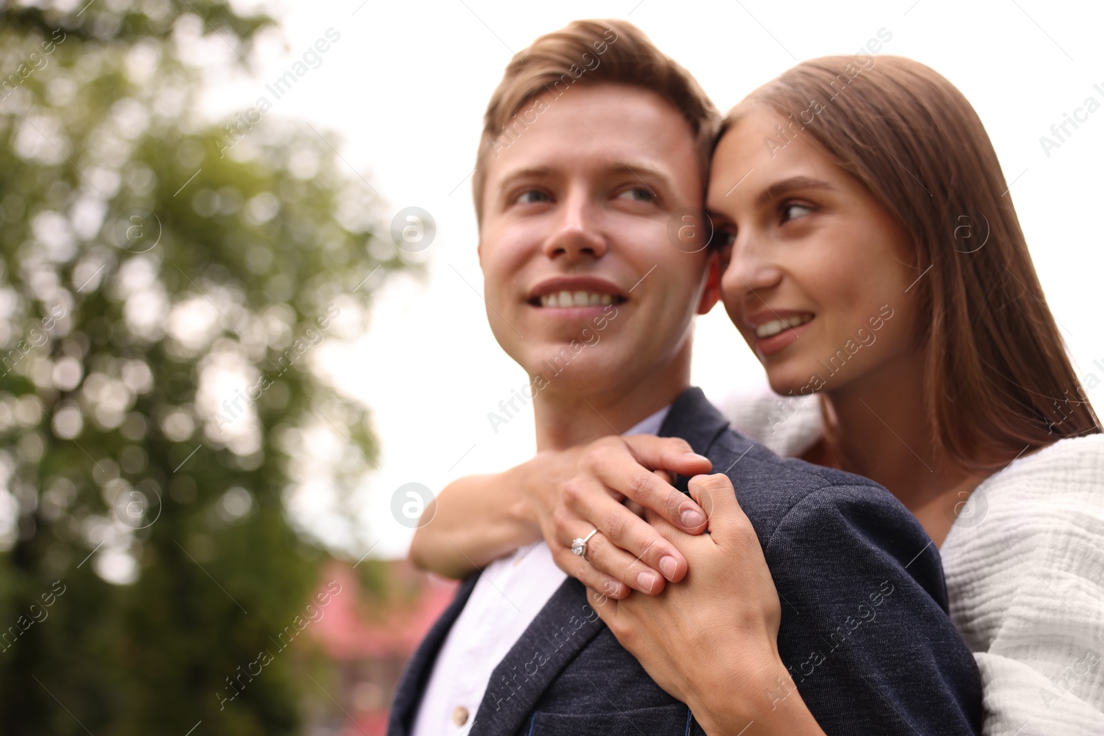 Marriage proposal. Woman with engagement ring hugging her smiling fiance outdoors, low angle view. Space for text Photo of Marriage proposal. Woman with engagement ring hugging her smiling fiance outdoors, low angle view. Space for text