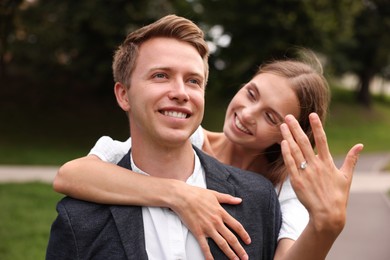 Photo of Marriage proposal. Smiling woman showing engagement ring and hugging her fiance outdoors