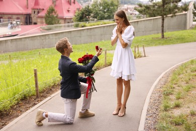 Photo of Man with engagement ring and bouquet of roses making marriage proposal to his happy girlfriend outdoors