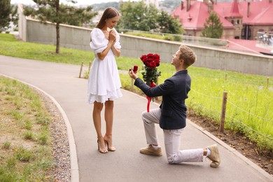 Photo of Man with engagement ring and bouquet of roses making marriage proposal to his happy girlfriend outdoors