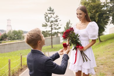 Photo of Man with engagement ring and bouquet of roses making marriage proposal to his happy girlfriend outdoors