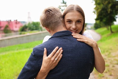 Photo of Marriage proposal. Smiling woman with engagement ring hugging her fiance outdoors
