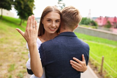 Photo of Marriage proposal. Smiling woman showing engagement ring and hugging her fiance outdoors