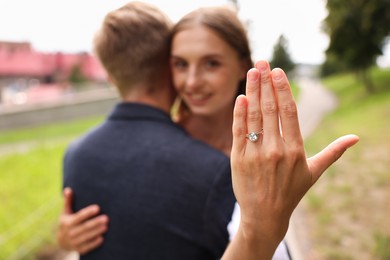 Photo of Marriage proposal. Smiling woman showing engagement ring and hugging her fiance outdoors, selective focus