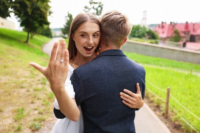 Photo of Marriage proposal. Excited woman with engagement ring hugging her fiance outdoors