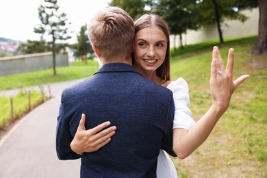 Photo of Marriage proposal. Smiling woman with engagement ring hugging her fiance outdoors
