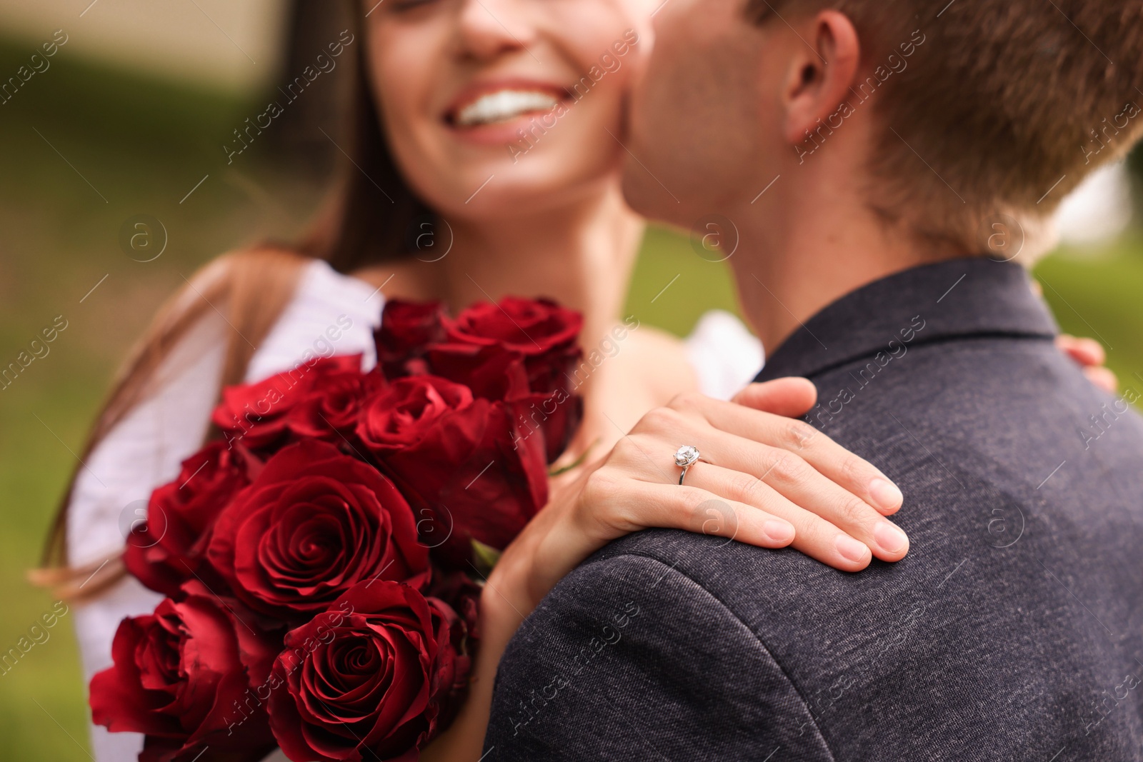Marriage proposal. Man kissing his beloved with engagement ring and bouquet of roses outdoors, selective focus Photo of Marriage proposal. Man kissing his beloved with engagement ring and bouquet of roses outdoors, selective focus