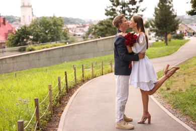 Photo of Marriage proposal. Man kissing his beloved with bouquet of roses on engagement day outdoors. Space for text