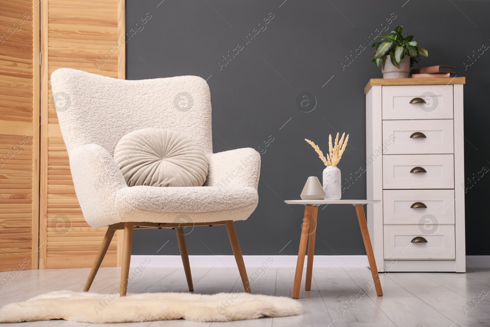 Photo of Contemporary armchair with pillow, side table and chest of drawers indoors. Interior design