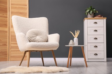 Photo of Contemporary armchair with pillow, side table and chest of drawers indoors. Interior design