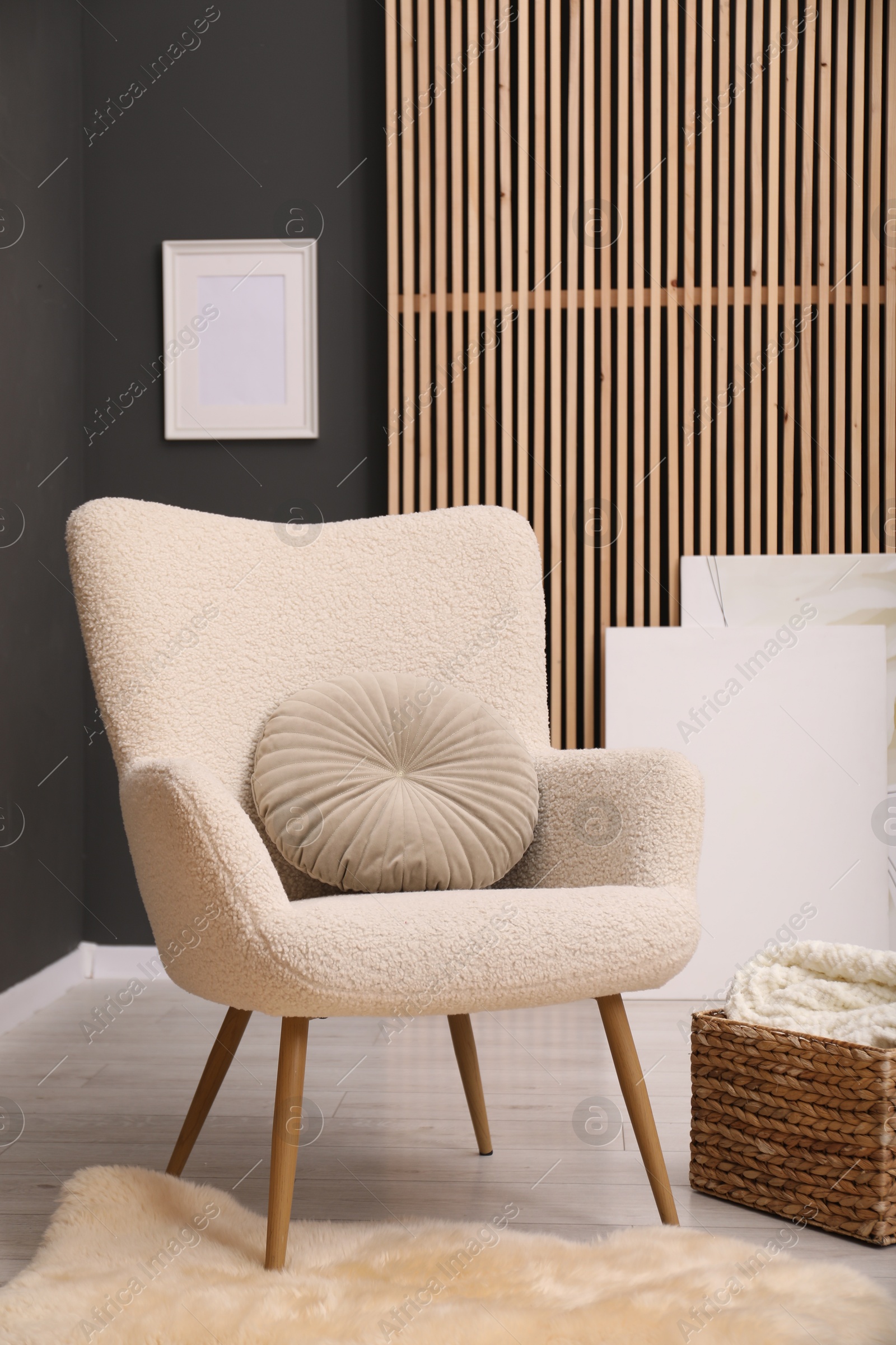 Photo of Contemporary armchair with pillow, rug and wicker basket indoors. Interior design