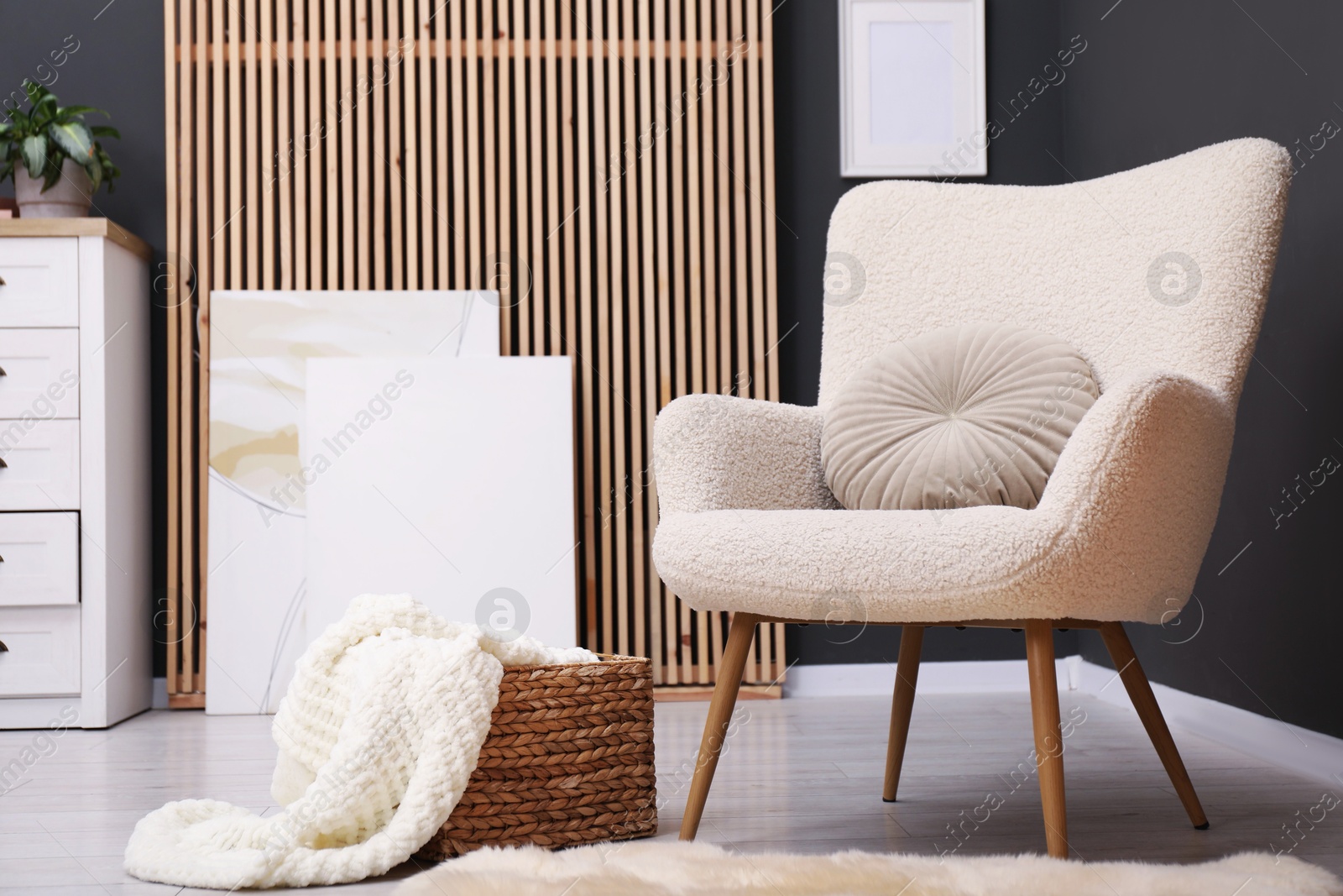Photo of Contemporary armchair with pillow, rug and wicker basket indoors. Interior design