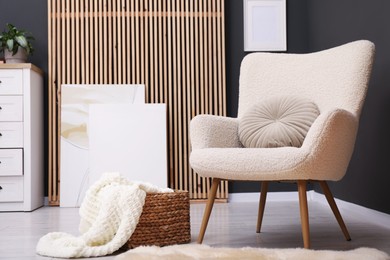 Photo of Contemporary armchair with pillow, rug and wicker basket indoors. Interior design