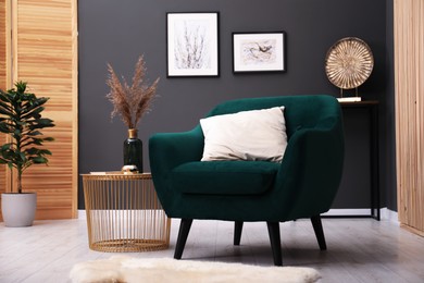 Photo of Contemporary armchair with pillow, rug and side table indoors. Interior design