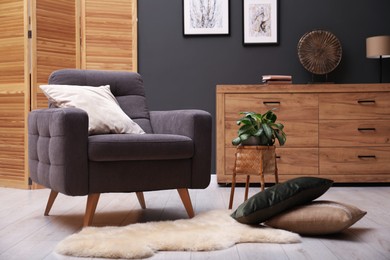 Photo of Contemporary armchair with pillow, rug and houseplant indoors. Interior design