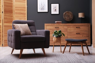 Photo of Contemporary armchair with pillow, bench and houseplant indoors. Interior design