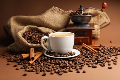 Photo of Cup of hot coffee, beans, grinder and cinnamon on brown background