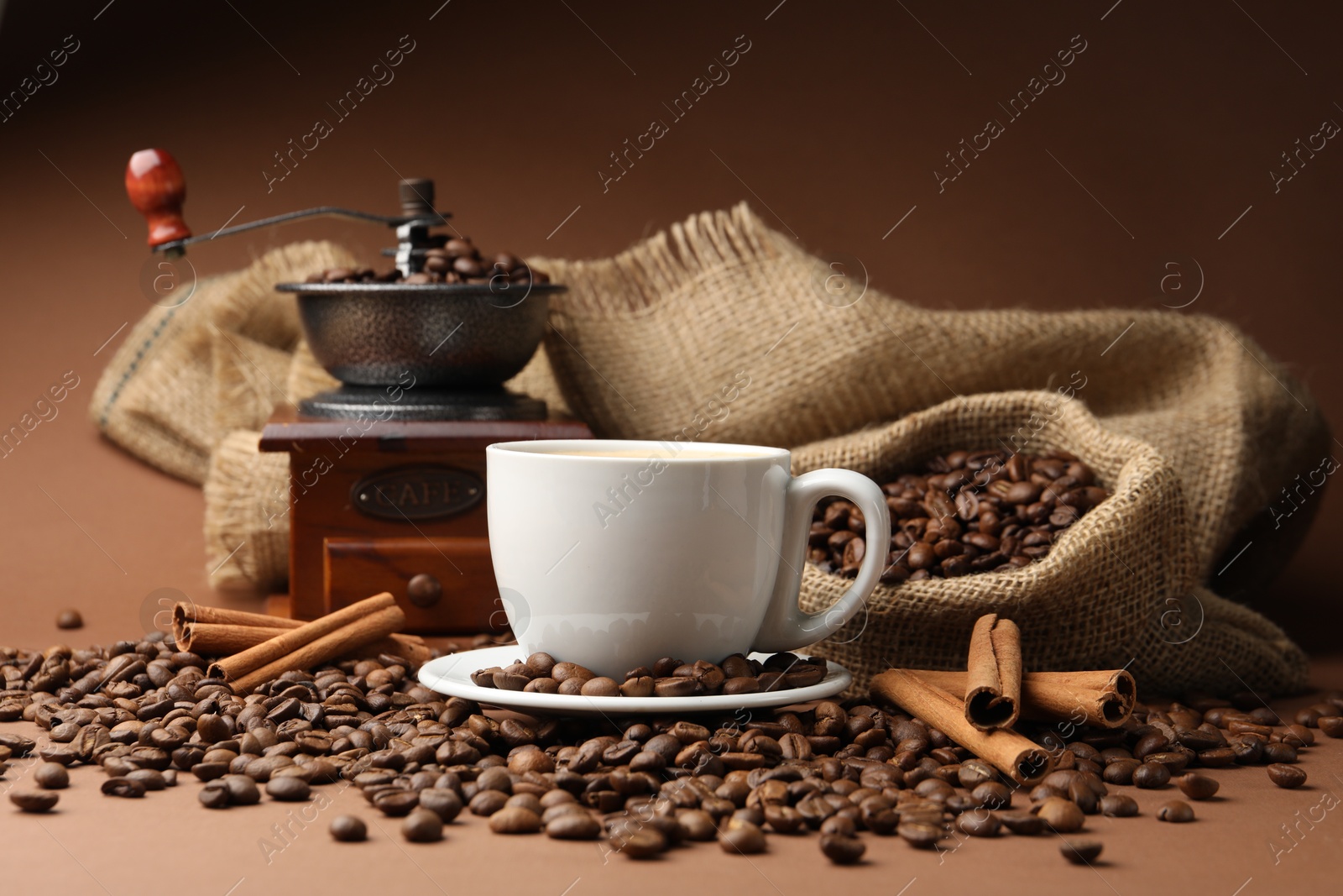 Cup of hot coffee, beans, grinder and cinnamon on brown background, closeup Photo of Cup of hot coffee, beans, grinder and cinnamon on brown background, closeup