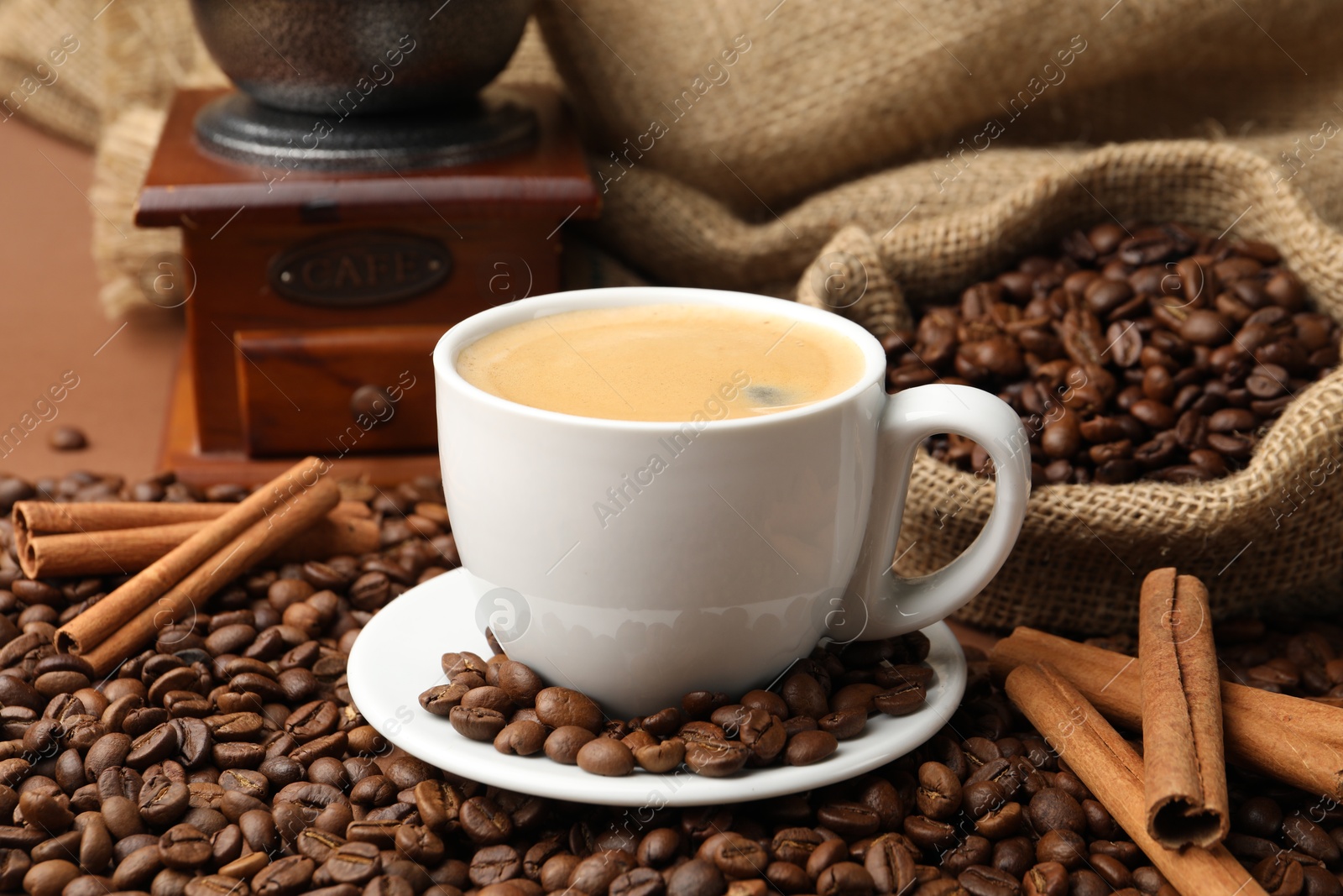 Cup of hot coffee, beans, grinder and cinnamon on brown background, closeup Photo of Cup of hot coffee, beans, grinder and cinnamon on brown background, closeup