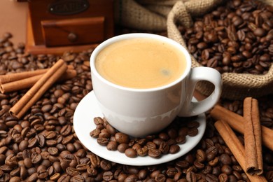 Photo of Cup of hot coffee, beans and cinnamon on brown background, closeup
