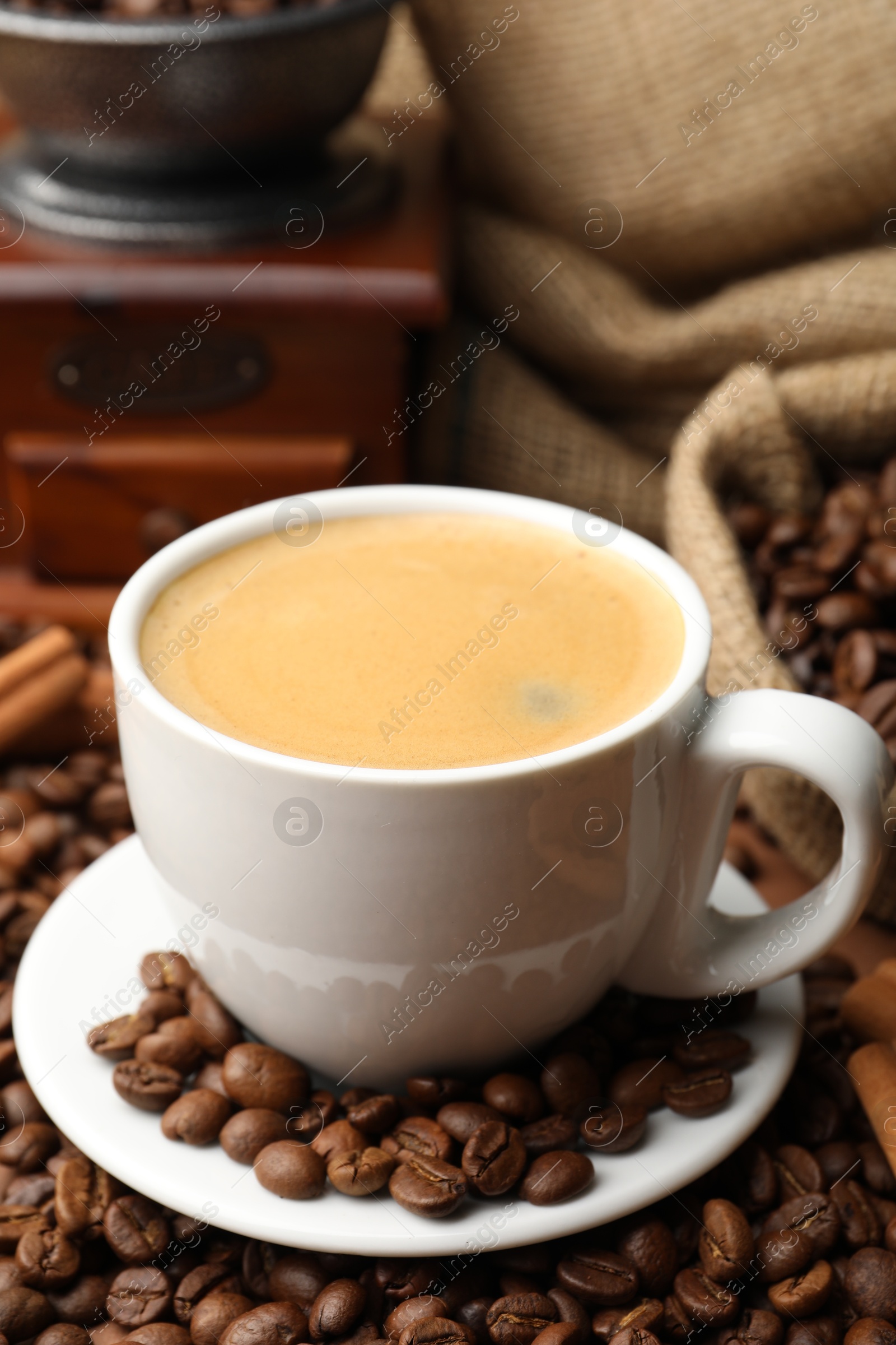 Cup of hot coffee, beans, grinder and cinnamon on brown background, closeup Photo of Cup of hot coffee, beans, grinder and cinnamon on brown background, closeup