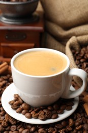 Photo of Cup of hot coffee, beans, grinder and cinnamon on brown background, closeup