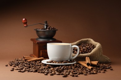 Photo of Cup of hot coffee, beans, grinder and cinnamon on brown background