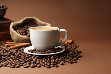 Photo of Cup of hot coffee, beans, grinder and cinnamon on brown background, closeup